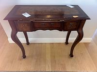 Front view of wooden sideboard showing three drawers with missing pulls and curved legs.
