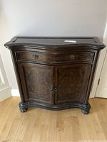 Front view of vintage wooden sideboard cabinet showing curved front, drawer, double doors with inlay and metal handles.