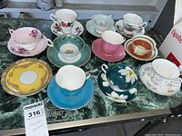 Wide view of 9 teacups and 10 saucers with various floral designs on a green marble surface.