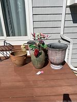 Wide shot of hanging ceramic vase with faux flowers flanked by two large plastic planters and two terra cotta planters on a back deck.