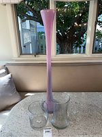 Three vases on a white speckled surface near window, showing overall lot with tall pink vase and two clear glass vases.
