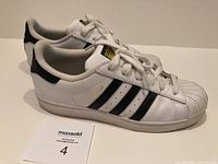 Side view of Adidas Superstar sneakers showing white leather upper and black stripes