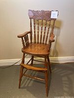 Full view of antique wooden toddler high chair showing carved backrest, armrests, and footrest.