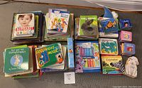 Stacks of multiple colorful baby board books including titles like Baby Alphabet, Discover Music, Baby Animals, Goodnight Moon, and Sandra Boynton's But Not the Hippopotamus.