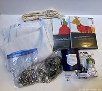 White textured shower curtain with metal grommets spread out, curtain rings in two plastic bags and loose, two packaged decorative pillowcases with Christmas designs, blue scented candle, botanical air freshener, and white macrame-style plant hanger on white background.