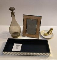 Full lot view showing all four items: smoked glass decanter, gold framed mirror picture frame, gold stiletto ring holder on white dish, and rectangular gold patterned black trinket tray.