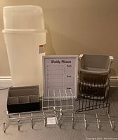 Photo of various home organization items on floor including weekly planner board, mail organizer, file folder organizers, and two over-the-door hangers with multiple hooks.