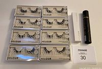 8 pairs of Velour Effortless no trim false lashes, white lash adhesive box, and black adhesive liner tube arranged on white surface