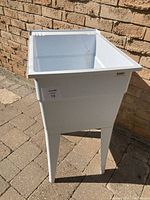 Laundry tub outdoors against brick wall, showing full front and side view including four legs and deep basin.