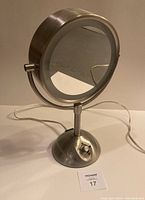 Front view of round light up makeup mirror on stand showing control switch and power cord.