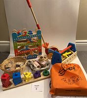 Photo showing the assortment of Montessori toys with the ball ramp in the back, wooden bird walker, toolbox, vintage blocks in a basket, wooden camera, shape sorter, and Skoolzy peg bag.