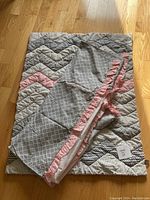 Reversible quilt folded showing chevron pattern in pink, grey, black, and white along with the crib skirt featuring a grey grid pattern and pink ruffles.