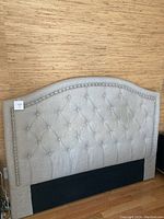 Full view of the gray upholstered headboard with tufted button design and black base with mounting hardware.