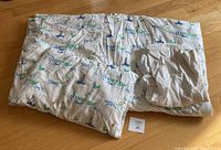 Toddler quilt folded alongside fitted sheet showing sailboat and animal themed pattern.