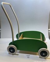 Side view of the IKEA Mula toddler walker wagon showing green wooden sides, natural wood seat, and curved metal handle.