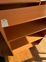 Top section and upper shelving of the wooden bookcase with light brown finish under natural light