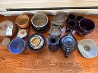 Overall view of the ceramic serveware collection arranged on wood floor showing mugs, bowls, teapot, and other pottery pieces.