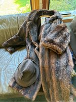 Brown fur coat with satin lining and a brown wool hat resting beside it on a couch under a window.