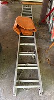 Full length view of the aluminum extension ladder laid flat on the floor with folded orange tarp on top.