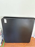 Two black folding tables stacked upright against a white wall, showing overall size and shape.