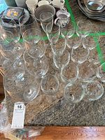 Multiple clear glass stemware including water and wine glasses arranged on kitchen counter with other kitchen items in background.