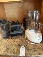 Overview of Vitamix blender base and container alongside Cuisinart food processor base with bowl and lid on countertop