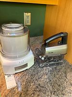 Cuisinart yogurt and ice cream maker next to Breville hand mixer with attachments on marble countertop