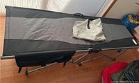 Full view of the portable folding cot unfolded on a wooden floor with carrying bag on top.