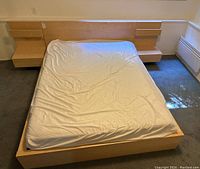 Full view of queen bed frame with mattress in a room, showing integrated headboard and attached nightstands on each side.