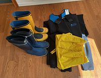 Photo showing the two pairs of rubber boots and two black/blue neoprene wetsuits with yellow rain gear jacket folded.