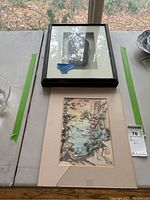 Two pieces of Asian art on table; one frame with broken glass, other unframed watercolor painting with mat.
