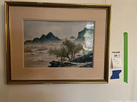 Overall view of framed ceramic landscape plaque with gilt frame and beige linen mat