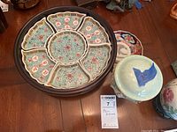 Set of Asian dishware including a sectioned serving plate and a blue covered pot on a wooden table