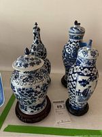 Four blue and white porcelain covered vases arrayed on table, showing shapes, patterns, and stands