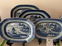 Four Blue Willow platters arranged on dark metal stands, full lot view