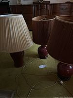 Three red ceramic table lamps with pleated shades displayed on floor