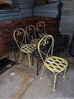 Ten metal ice cream parlor style chairs in black and yellow colors, showing the lot composition and condition in a basement with concrete floor and brick wall.