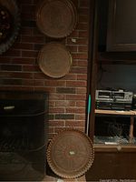 Three metal decorative plates arranged vertically against a brick wall and fireplace, showing the entire lot in situ.