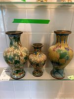 Front view of three metal cloisonné vases with floral and ornamental patterns.