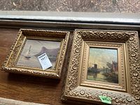 Two framed oil paintings on a wood surface near a window