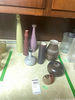 Eight pottery vases of various sizes and colors displayed on a countertop, showing chipping and wear on surfaces.