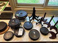 Overview of various wooden display stands laid out on a surface near a window, showing different styles including round bases and easel supports.