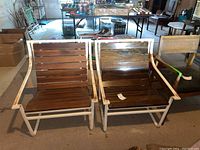 Front view of two vintage metal frame chairs with wooden slats in basement setting showing rust and wear.