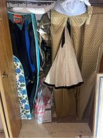 Closet with vintage clothing hanging in quilted garment bags, showing a beige skirt and assorted jackets with visible dust and dirt.