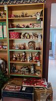 Front view of the laminate wood bookshelf filled with various holiday and decorative figurines. Shows six shelves, some decorated with faux snow trees and snow globes. Shelf surfaces and sides visible, showing wood laminate material.