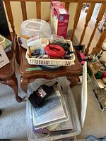 Photo of plastic basket on wooden table containing cake decorating tools and candy moulds, metal baking pans underneath, black apron, and other assorted baking supplies.