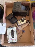 Box containing the Canon camera with wrist strap, Tasco binoculars in case, GE cassette player with earbuds