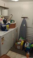 Laundry room with washing machine, dryer, clothes baskets, ironing board, and drying rack.