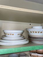 Stack of Corelle plates and bowls with yellow-gold floral pattern on white background