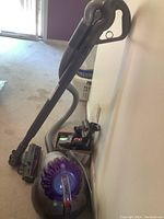 Dyson Big Ball Animal vacuum main unit with hose and wand leaning against wall alongside attachments.